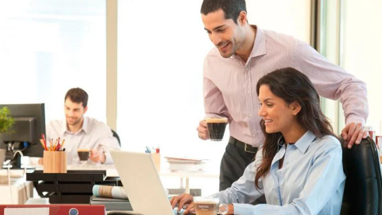 Compañeros de trabajo comentando asuntos y bebiendo café en la oficina