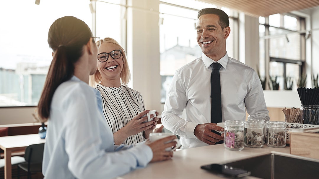 Un hombre y dos mujeres ríen mientras toman café