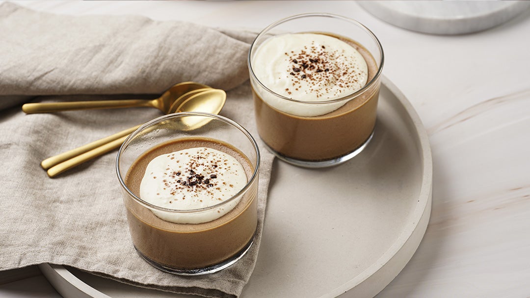 Dos vasos con natilla de chocolate encima de un plato con un mantel y 3 cucharas