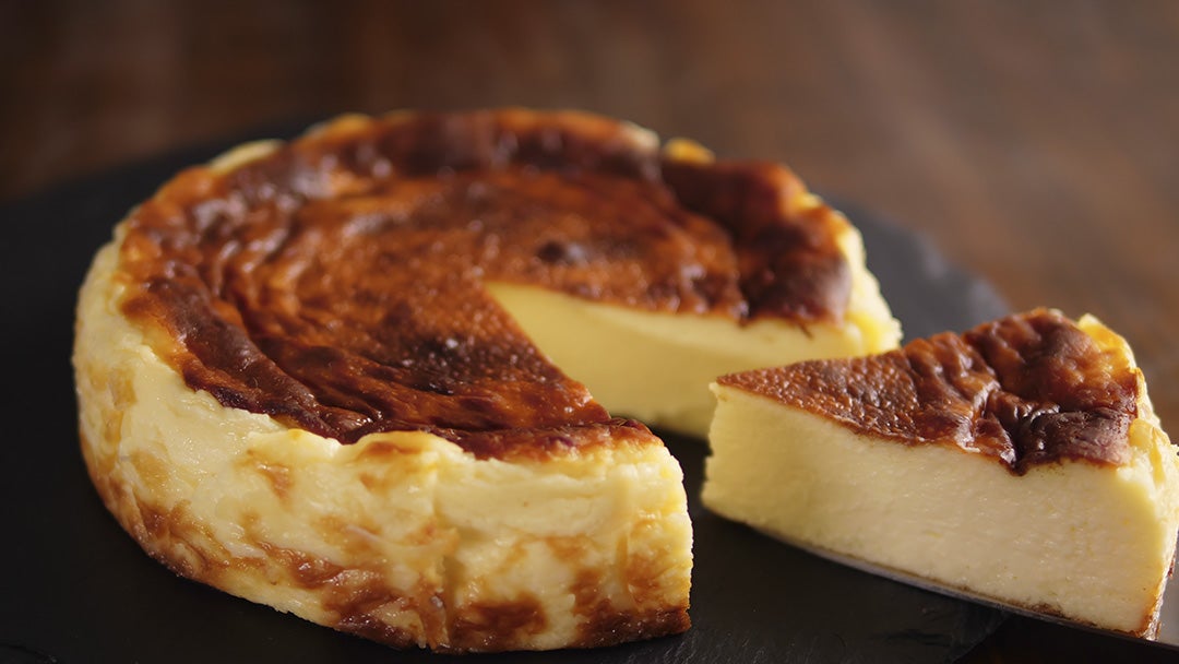 Tarta de queso horneada en un plato negro, con una porción removida revelando el centro cremoso.
