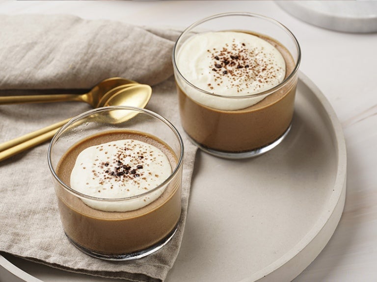 Dos vasos con natilla de chocolate encima de un plato con un mantel y 3 cucharas