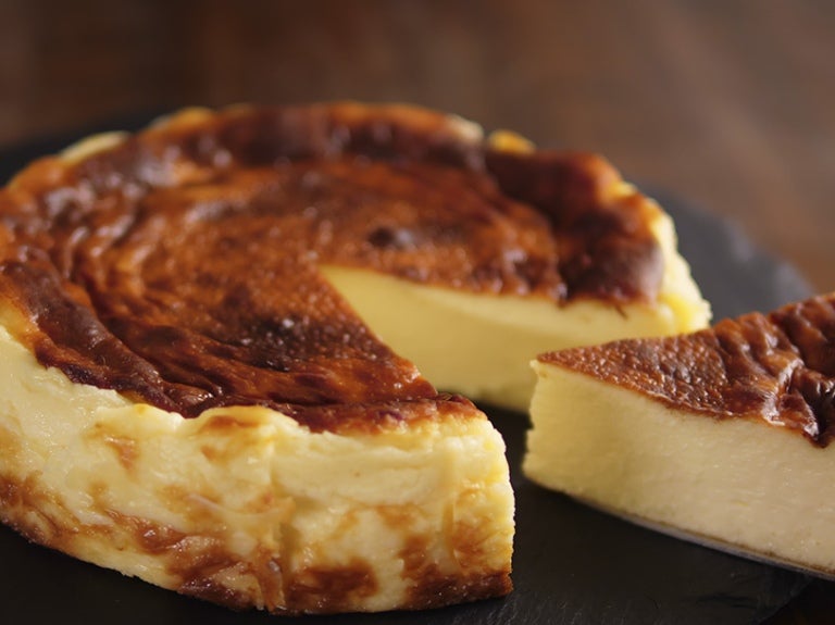 Tarta de queso horneada en un plato negro, con una porción removida revelando el centro cremoso.